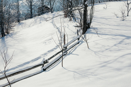 覆盖着雪帽的木栅栏。 冬季乡村风景村或农场晴天蓝影山和森林背景