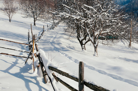 覆盖着雪帽的木栅栏。 冬季乡村风景村或农场晴天蓝影山和森林背景