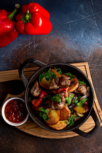 在黑色背景的轻质木板上, 用烤牛肉和土豆烤蔬菜和青菜煎锅。背景是用蔬菜装饰的