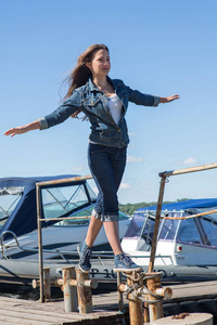 一个欧洲貌美的女孩站在一个木墩上。 夏日。 大风。 在蓝天上发展一个女孩的身材。