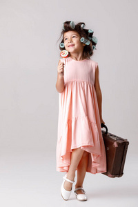 滑稽的小女孩在粉红色的礼服和卷发拿着棒棒糖