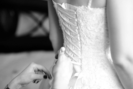 s hands tie a ribbon on the corset of a wedding dress. Black and