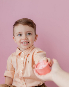 带着礼物的快乐小男孩。 照片隔离在粉红色背景上。 微笑的男孩拿着礼物盒。 假期和生日的概念。