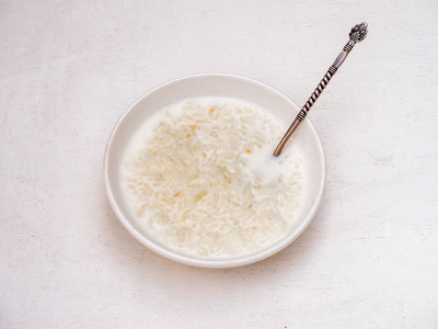 牛奶米粥在一个深盘子里，里面有一个老式的勺子。 盘子在白色的桌子上。