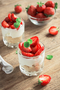 草莓甜点，奶油奶酪和新鲜草莓在木制背景。 健康自制草莓芝士蛋糕眼镜。
