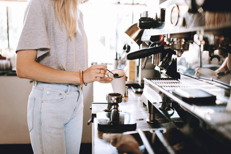 一位年轻的瘦金发碧眼的女士, 穿着休闲的衣服, 站在舒适的咖啡店里的咖啡机旁边