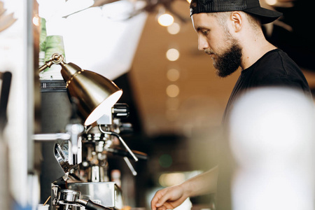 一个带着胡子的时尚年轻人, 穿着休闲服, 在现代化的咖啡店里的咖啡机里煮咖啡