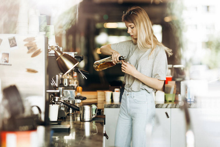 一个年轻的漂亮的金发碧眼, 穿着休闲装, 正在一家现代化的咖啡店煮咖啡。咖啡的制作过程如下