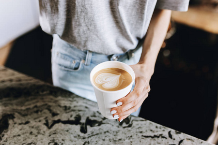一个年轻苗条善良的金发女孩, 穿着休闲装, 巧妙地添加牛奶到咖啡在一个现代化的咖啡店