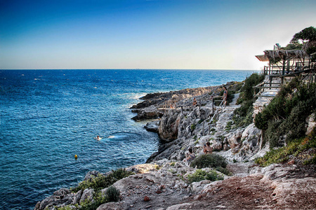 日落在清澈的大海附近浪漫的岩石悬崖上。 人们在海里游泳，跳进水里。 它位于希腊Zakynthos的波尔图罗沙海滩。