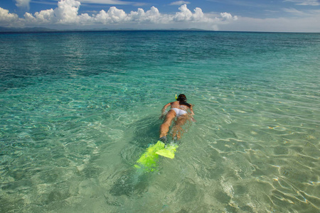 年轻女子在热带岛屿附近清澈的浅水中浮潜