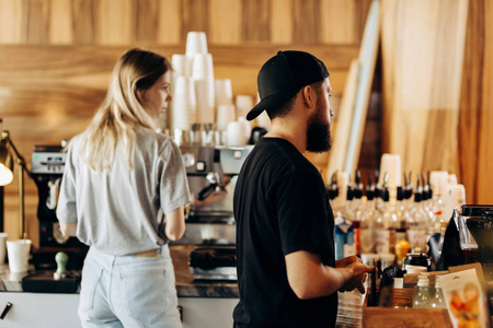 两个年轻的时尚的人, 一个瘦瘦的金发女孩和一个留胡子的男人, 穿着随意的紧身衣, 在一家现代化的咖啡店煮咖啡