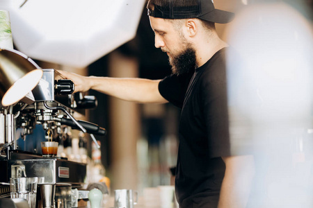 一个穿着休闲服的时尚年轻人, 在舒适的咖啡店里的咖啡机里煮咖啡