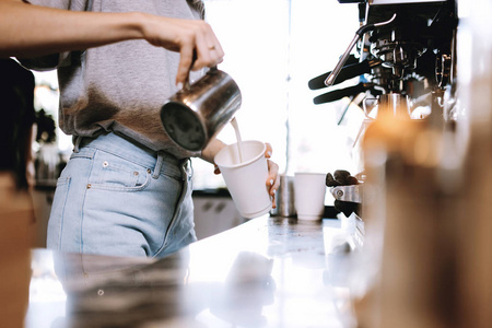 在一家舒适的咖啡店里, 一个年轻的瘦金发女孩穿着休闲外套, 在咖啡中加入牛奶