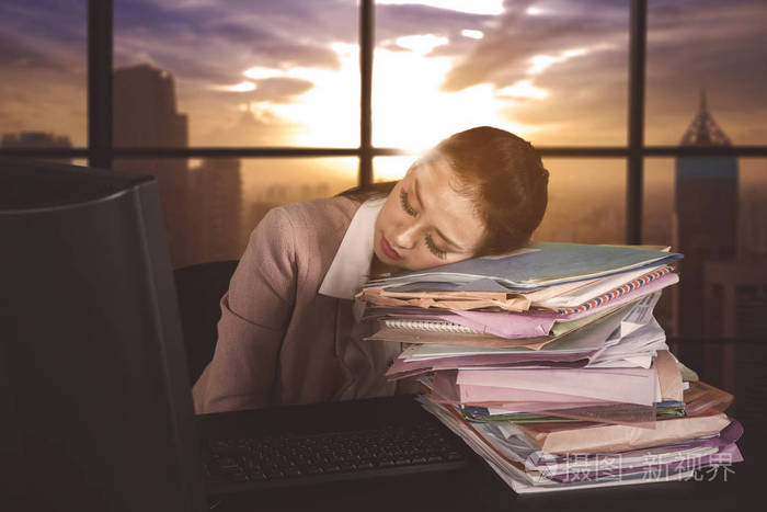 过度劳累的女企业家的形象睡在办公室的一堆文件之上. 黄昏时分拍摄