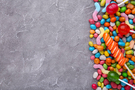 彩色棒棒糖和不同颜色的圆形糖果在灰色混凝土背面
