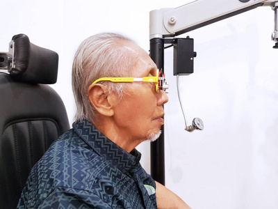 在眼科医生检查近视眼睛时，使用眼镜光镜的老人的侧视