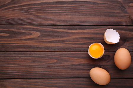 鸡蛋和半个蛋黄在棕色背景上。 棕色木桌上的鸡蛋