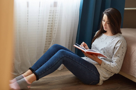 地板上放松,看书,穿着毛衣,牛仔裤和袜子,因为集中的表情喜欢她的爱好