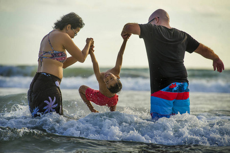 年轻快乐的混血儿夫妇白种人男子和亚洲印度尼西亚妇女在热带海滩玩耍，小儿子父母抚养孩子在海水之上，在假期旅行中玩得开心