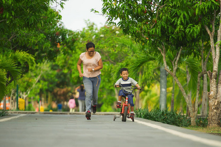 生活方式肖像亚洲印度尼西亚母亲和年轻快乐的儿子在城市公园一起玩，孩子学习骑自行车，女人在母亲的概念中追逐孩子