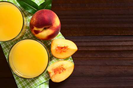 桃汁或花蜜杯中的新鲜成熟的桃果子在头顶的深色木材上拍摄，自然光线选择性聚焦在果汁的顶部和整个水果的顶部
