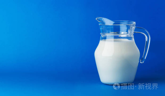 在蓝色背景上被隔绝的牛奶的玻璃水罐与拷贝空间