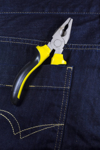蓝色牛仔裤口袋里的黄色钳子。 一般修理用的钳具。 建筑物