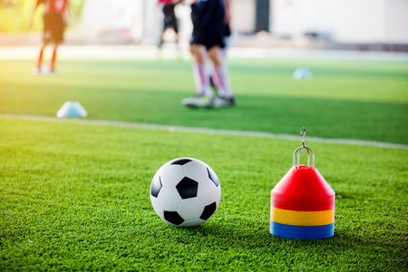 足球和锥标记在绿色人造草坪上，足球运动员训练模糊。 足球学院