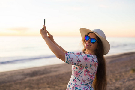 旅行者年轻女子正在用手机摄像头拍摄美丽的日落风景视频。暑假旅游和度假