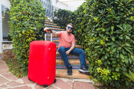 旅行旅游和假期的概念快乐的人坐在楼梯上, 拿着红色的手提箱在阳光明媚的眼镜上