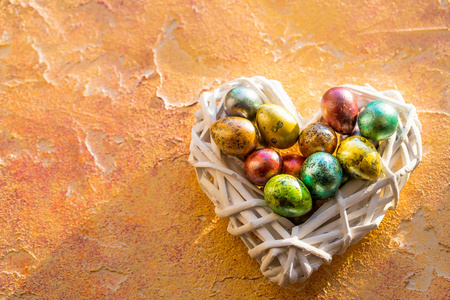 复活节快乐。橙色桌子上有五颜六色的鸡蛋和复活节装饰, 有复制空间。复活节彩蛋在装饰巢在心脏形状。闪亮的颜色鹌鹑复活节蛋天主教和正