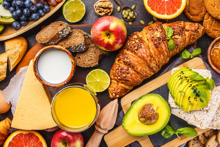健康平衡的早餐在黑暗的背景下。 梅斯利牛奶，牛角面包，奶酪，饼干和水果的顶部视图。
