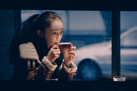 亚洲年轻女性独自坐在咖啡厅饮料桌城市窗口中喝酒