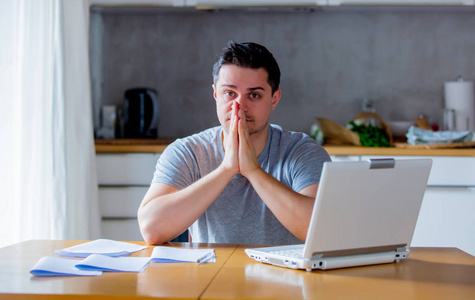 心烦意乱的年轻人在网上找工作，坐在厨房里拿着笔记本电脑。
