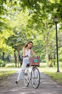 亚洲黑发有趣的女人腿在公园骑自行车，阳光和树叶背景在夏天。 女孩健康和运动的生活方式概念。