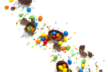 碎的和整个巧克力复活节彩蛋，白色背景上的五彩糖果。庆祝复活节的概念，复活节装饰品，寻找复活节兔子的糖果。平躺，俯视。复制空间