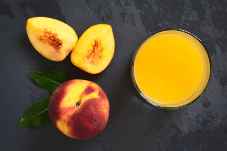 桃汁或花蜜在玻璃中与新鲜成熟的桃果放在一边，用自然光在石板上拍摄选择性聚焦在果汁的顶部和整个水果的顶部