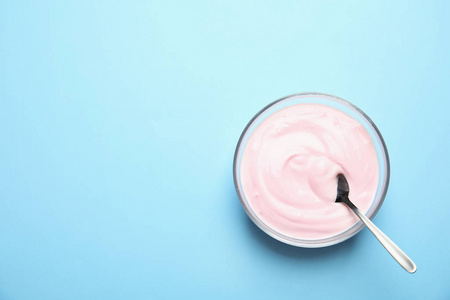 玻璃碗与奶油酸奶和勺子的颜色背景顶部视图。 文本空间