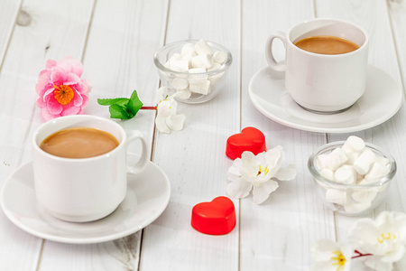 两颗装饰的心和两杯咖啡，背景是一张浅色的桌面和人造花的甜点