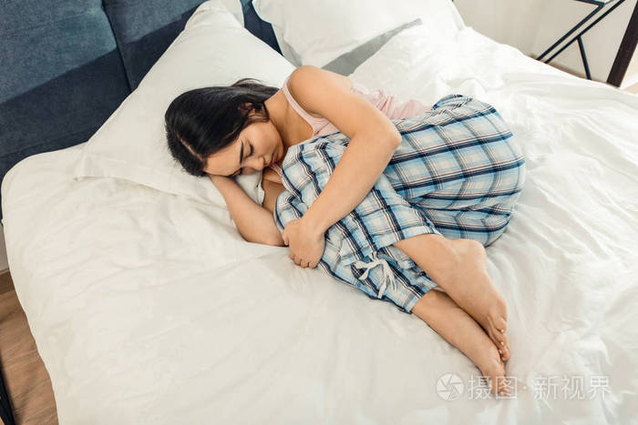 苗条的黑发女人抱着她的膝盖, 而躺在床上