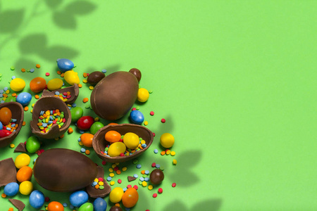 碎的和整个巧克力复活节鸡蛋，五颜六色的糖果在绿色的背景。 灌木。 庆祝复活节复活节装饰品的概念。 平躺顶部视图。 复制空间。