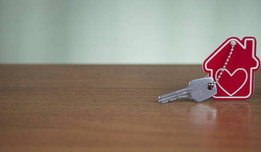 房屋钥匙在房子上，形状的钥匙链，放在木桌上，用于房地产搬迁或租赁财产的概念