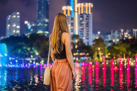 妇女游客在背景五颜六色的喷泉在湖在晚上, 靠近双子塔与城市的背景。吉隆坡, 马来西亚