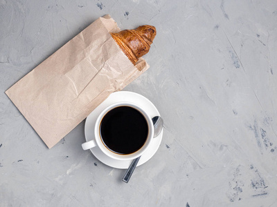 咖啡杯和羊角面包在纸包装上的灰色石头背景上的桌子上。早上的早餐很丰盛。质朴的风格, 顶视图