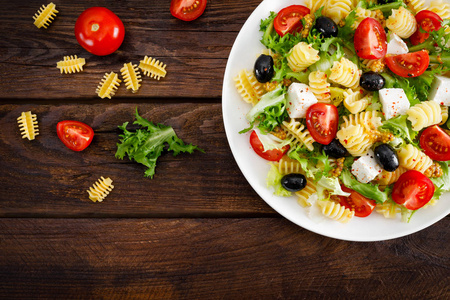 意大利面食沙拉与新鲜番茄奶酪生菜和橄榄木背景。 地中海美食。 做午餐。 健康饮食食物