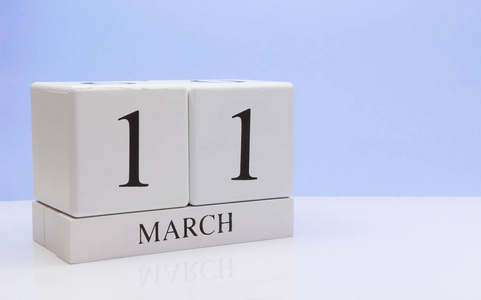 三月十一日。 月11日每日日历在白色桌子上，反射浅蓝色背景。 春天的时间，空的文字空间