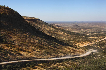 车辆沿着一条尘土飞扬的偏远沙漠道路行驶，穿过纳米比亚的达马拉兰。