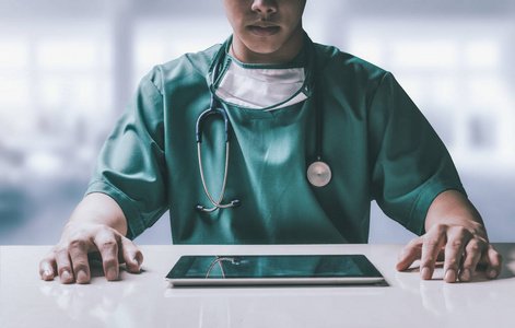 外科医生坐在医院办公室的桌子上，拿着平板电脑。医疗保健人员和医生服务。
