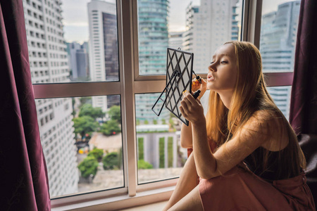 年轻女子坐在窗边化妆, 可以看到摩天大楼和大城市的全景